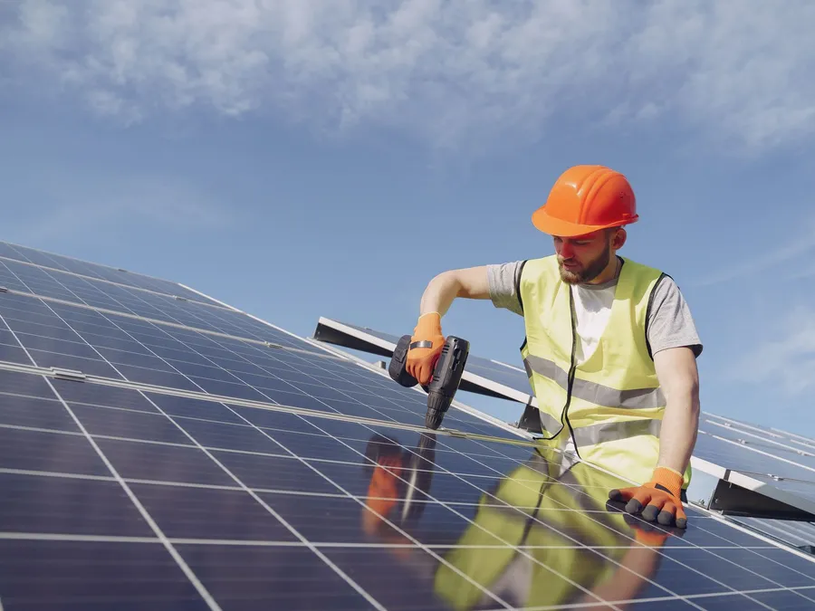 Technician using a drill to fix solar mounting against the sky, illustrative photograph